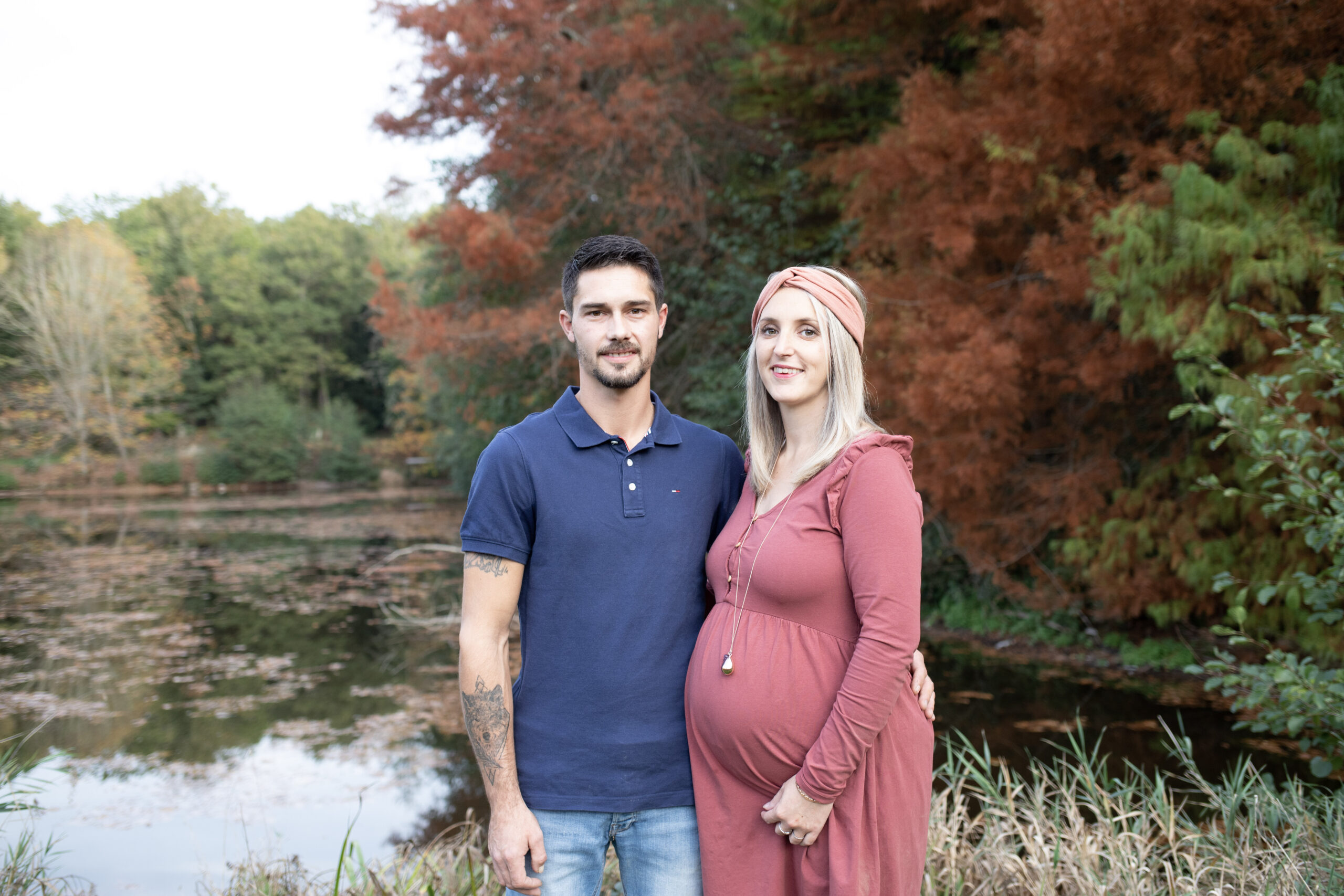 Futurs parents posant au bord d'un étang aux couleurs d'automne